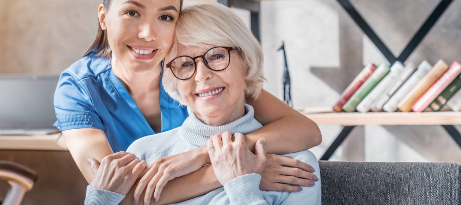 Portrait of female caretaker hugging happy elderly woman indoors