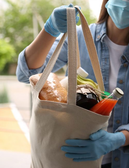 Female volunteer giving bag with products through doorway, closeup. Aid during coronavirus quarantine