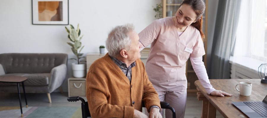 Portrait of smiling female nurse helping senior man in wheelchair at retirement home, copy space