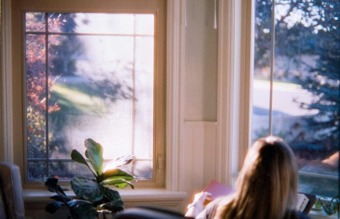A person sits beside a bright window with a book