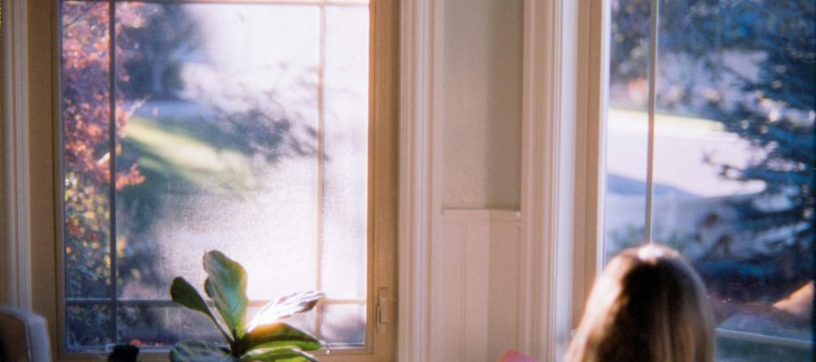 A person sits beside a bright window with a book