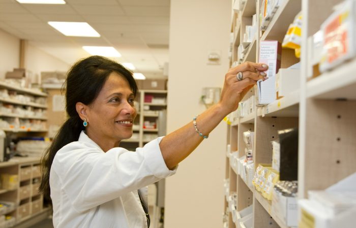 A pharmacist reaches for a medicine on a pharmacy shelf