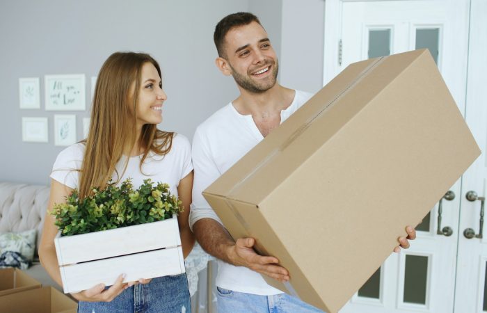 Two adults carry a cardboard box into a new home