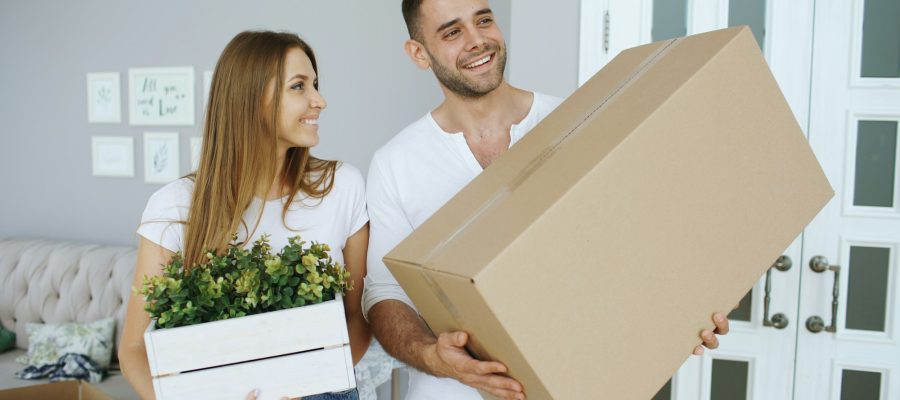Two adults carry a cardboard box into a new home