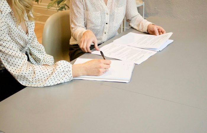 Two women review and sign a document at a table