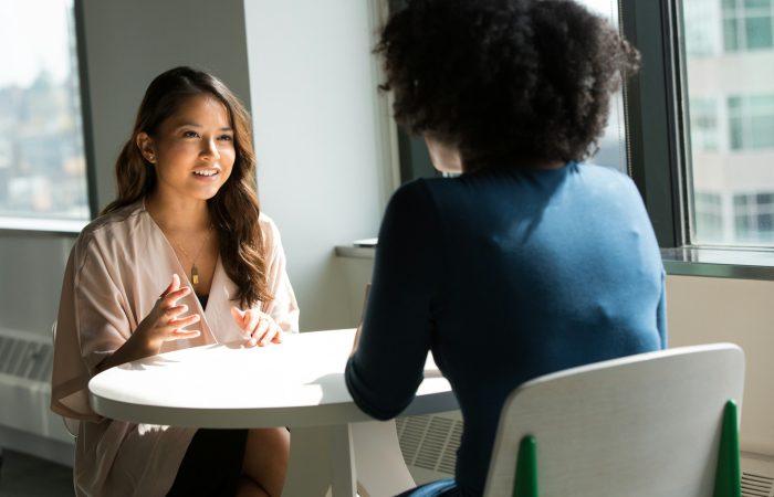 Two women talk together while seated in a bright room