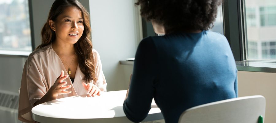Two women talk together while seated in a bright room