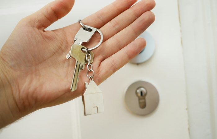 A hand holds house keys beside a door lock