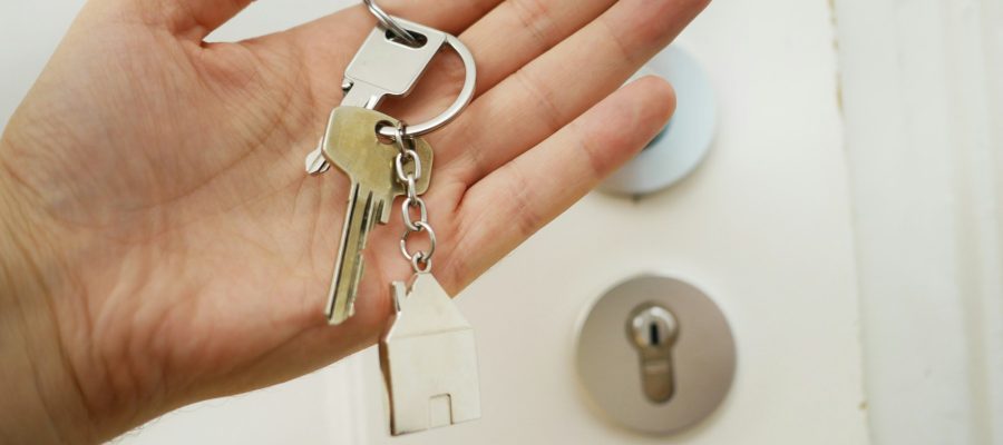 A hand holds house keys beside a door lock
